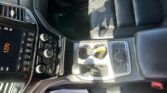 Interior of a car showing the center console with a touchscreen, climate controls, and cup holders next to a leather seat.