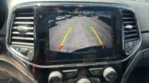 Car infotainment screen showing rear‑view camera with guiding lines in a parking lot; text reads 'Check Entire Surroundings'