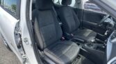 Front interior of a white car with two black patterned cloth seats, driver’s door open.