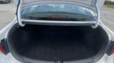 Open trunk of a white sedan showing a dark cargo area and rear windshield with other cars in the parking lot behind it