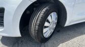 Close-up of a silver car's front left wheel and tire, with the wheel well and bumper in view on asphalt.