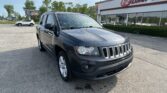 Front-right/foreground view of a dark gray Jeep SUV (Grand Cherokee) parked in a dealership lot, with EZ Loan Auto storefront in the background.