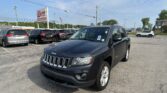 Front-right view of a dark blue Jeep SUV in a car dealership lot, with other vehicles, a tall EZ LOAN Auto Sales sign, and an American flag in the background.