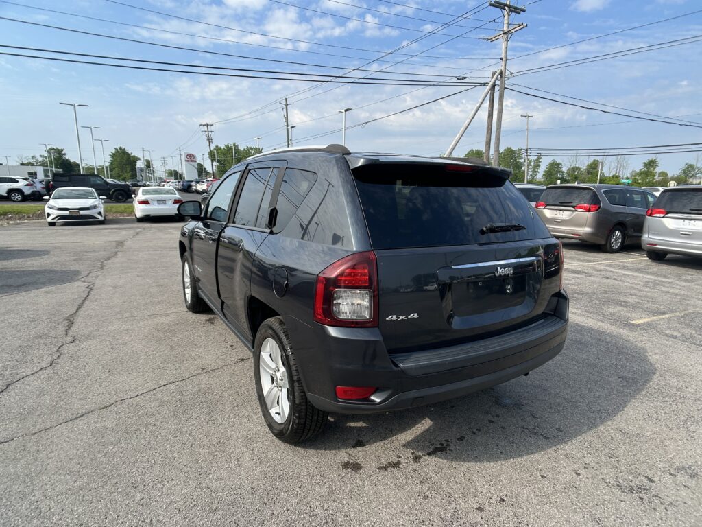 Rear three-quarter view of a dark blue/black Jeep SUV in a dealership parking lot with power lines overhead and other cars in the background.
