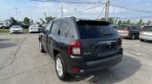 Rear three-quarter view of a dark blue/black Jeep SUV in a dealership parking lot with power lines overhead and other cars in the background.