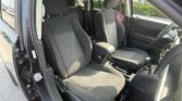 Front interior of a dark SUV with two black cloth seats, center console, gear shifter, and an open driver-side door.