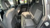 Back seat area of a dark fabric car with front seats visible, headrests, three seat belts, and cup holders on the floor nearby, as seen in a parking lot outside the window.