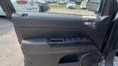 Interior of a car door panel with window controls and a chrome door handle; outside shows a parking lot with cars and a side mirror reflecting vehicles.