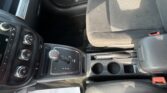 Front interior of a car showing the center console with gear shifter, cupholders, climate controls, and a paper on the passenger-side floor mat.
