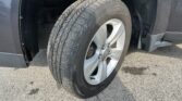 Close-up of a tire mounted on a silver alloy wheel, with the car's dark fender and wheel well in view on asphalt.