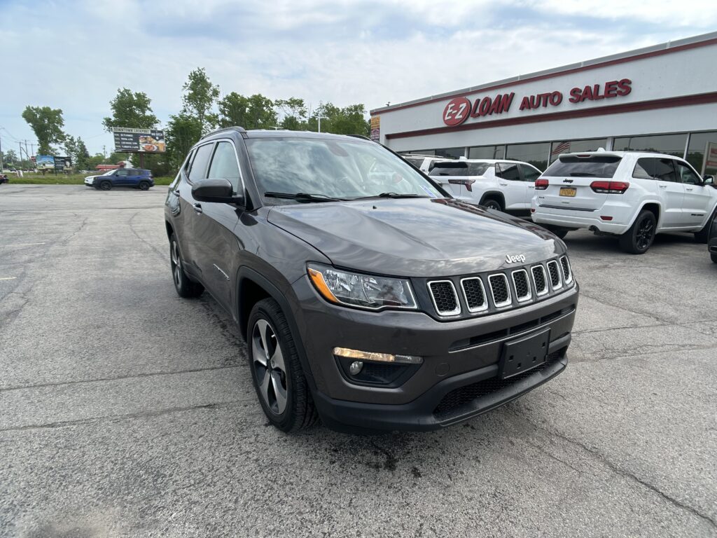 Front view of a gray Jeep SUV parked in a lot in front of the EZ Loan Auto Sales storefront with a red sign above the building.