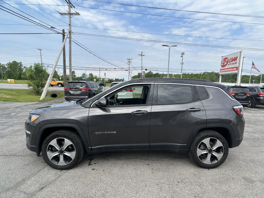 Gray Jeep Compass SUV in a dealership lot with power lines overhead and an EZ Loan Auto Sales sign in the background.