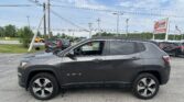 Gray Jeep Compass SUV in a dealership lot with power lines overhead and an EZ Loan Auto Sales sign in the background.