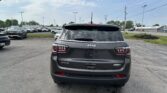 Rear view of a gray Jeep SUV (4x4 Latitude) parked in a car lot with other vehicles around and power lines overhead.