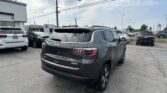 Black Jeep Grand Cherokee SUV in a car dealership lot, with other vehicles and a Toyota dealership building in the background.