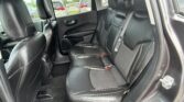 Rear seating area of a car with black leather seats, headrests, and visible seat belts in a parked lot outside the windows.