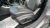 Front passenger seat and center console in a dark leather car interior with orange stitching and a seat belt visible.
