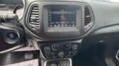 Center-dashboard view of a car’s infotainment screen showing radio options, with two air vents on either side and a flyer on the passenger floor reading “We Take Pride in Your Vehicle.”