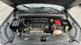 Open car hood revealing engine bay with exposed battery, coolant reservoir, and various hoses and components visible under the hood.