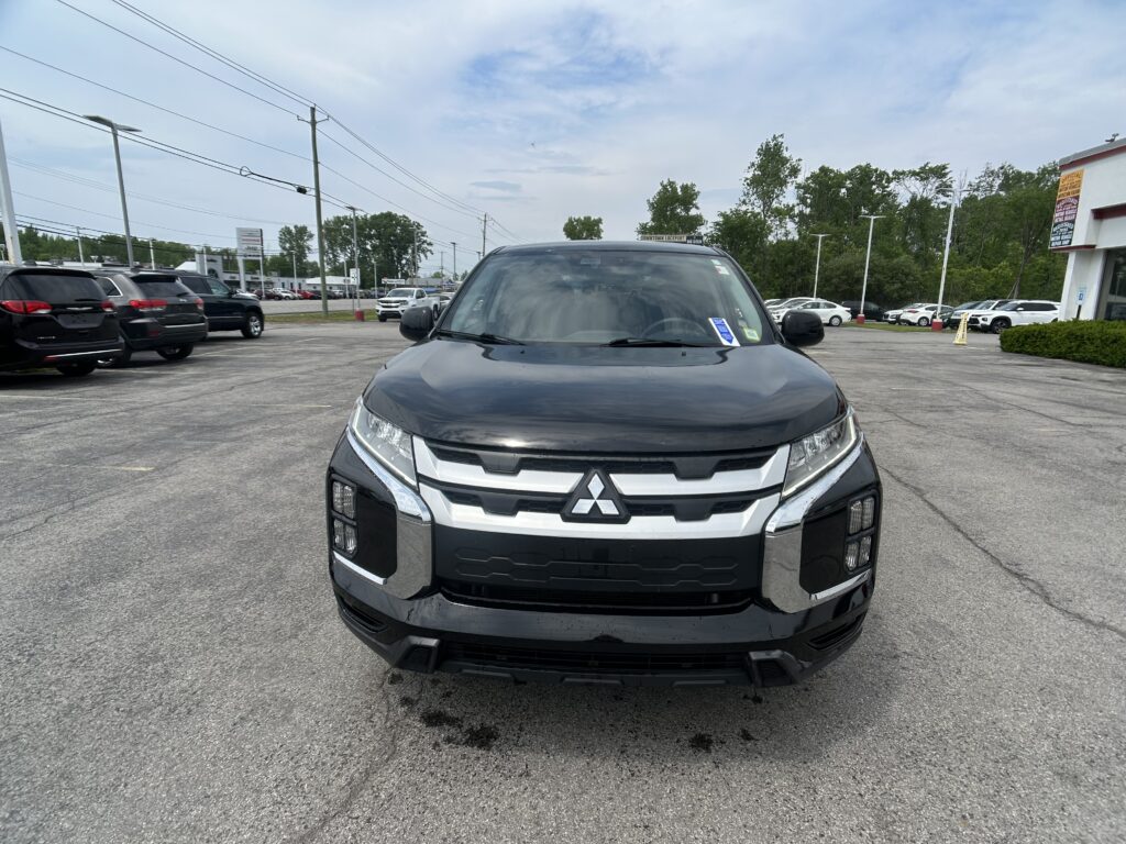 Front-facing view of a black Mitsubishi SUV in a car dealership lot, with other cars and a building in the background similarities in view consistent.