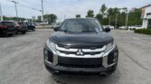 Front-facing view of a black Mitsubishi SUV in a car dealership lot, with other cars and a building in the background similarities in view consistent.