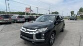 Black SUV in the foreground at a car dealership lot with several vans and a sign reading EZ-Loan Auto Sales in the background, plus an American flag nearby.