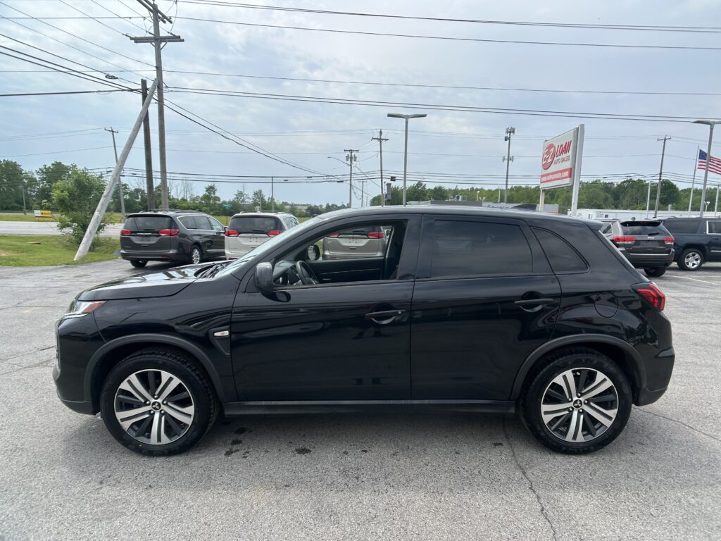 Shiny black SUV in the foreground at a car dealership lot, with vans, power lines, and an EZ LOAN sign in the background.