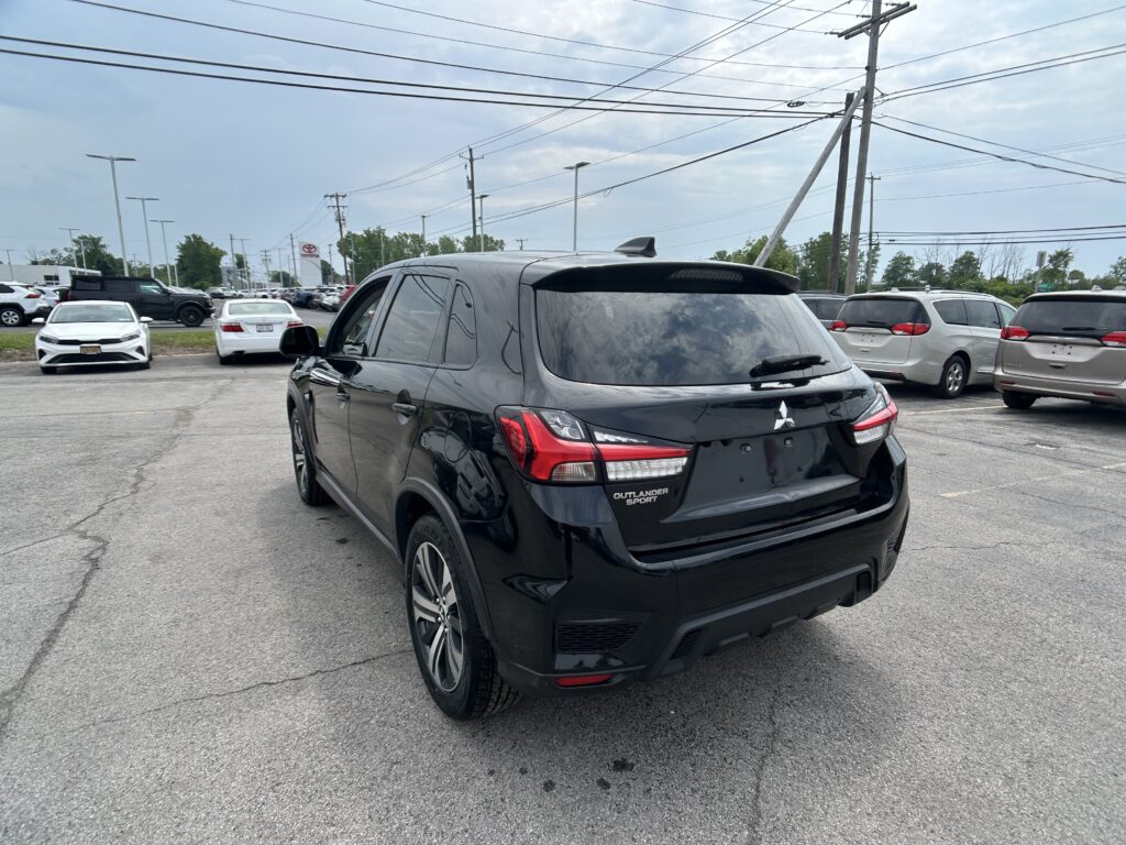 Rear three-quarter view of a black Mitsubishi Outlander Sport in a crowded car dealership lot with other vehicles nearby and power lines overhead.