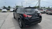 Rear three-quarter view of a black Mitsubishi Outlander Sport in a crowded car dealership lot with other vehicles nearby and power lines overhead.