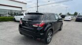 Black SUV in the foreground at a car dealership lot, with other cars and a white showroom on the left.