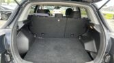 Rear cargo area of an SUV with rear seats upright and dark carpet, ready for loading. A seatbelt sits across the back row; vehicles are visible in the parking lot through the rear window.