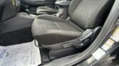Interior of a car showing the front seats, center console, and gear shifter from the passenger side. - Black cloth seats with a geometric stitching pattern and light-colored piping. - Dark floor mats and a protective paper mat on the floor near the door.