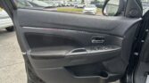 Close-up of a black car door interior with window control buttons; outside is a crowded parking lot with many cars.