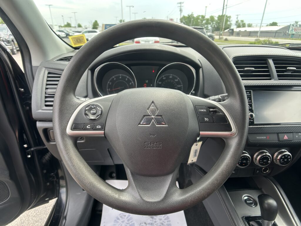 Close-up of a car steering wheel and dashboard from the driver's seat, with the speedometer and controls visible around it.