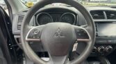 Close-up of a car steering wheel and dashboard from the driver's seat, with the speedometer and controls visible around it.
