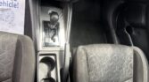 Center console of a car with gear shifter, cup holders, and climate controls visible, passenger seat to the right and a 'Pride Vehicle' sign on the left.