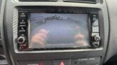 Infotainment screen shows a rearview camera feed with green guiding lines and the warning text 'Check surroundings for safety' at the bottom of the display in a car interior.