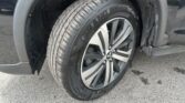 Close-up of a vehicle's front wheel: tire labeled GrandSport on a silver alloy rim with a dirt-splattered wheel well nearby.