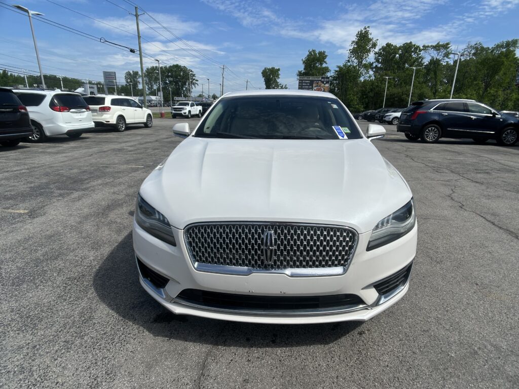 Front view of a white Lincoln SUV in a car dealership lot, with other vehicles parked nearby and a blue sky above.