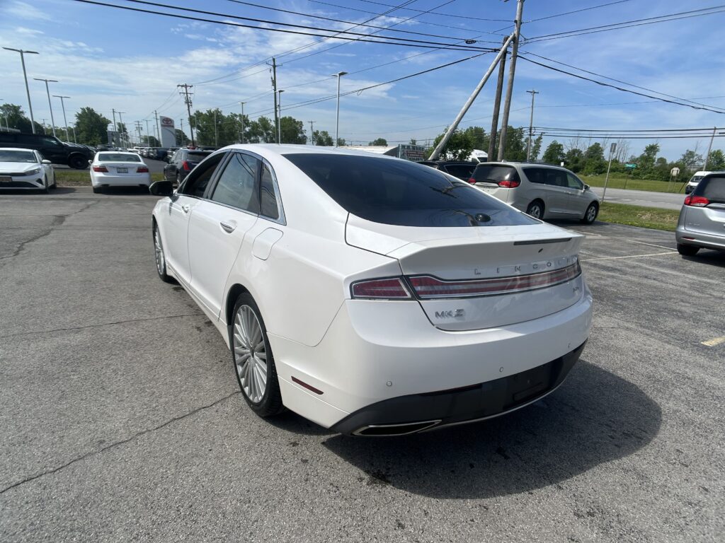 White Lincoln MKZ viewed from the rear side in a crowded parking lot with other cars and power lines overhead.