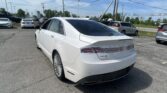 White Lincoln MKZ viewed from the rear side in a crowded parking lot with other cars and power lines overhead.