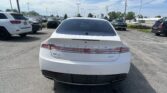 Rear view of a white Lincoln MKZ parked in a busy lot with other cars and overhead power lines in a clear sky.