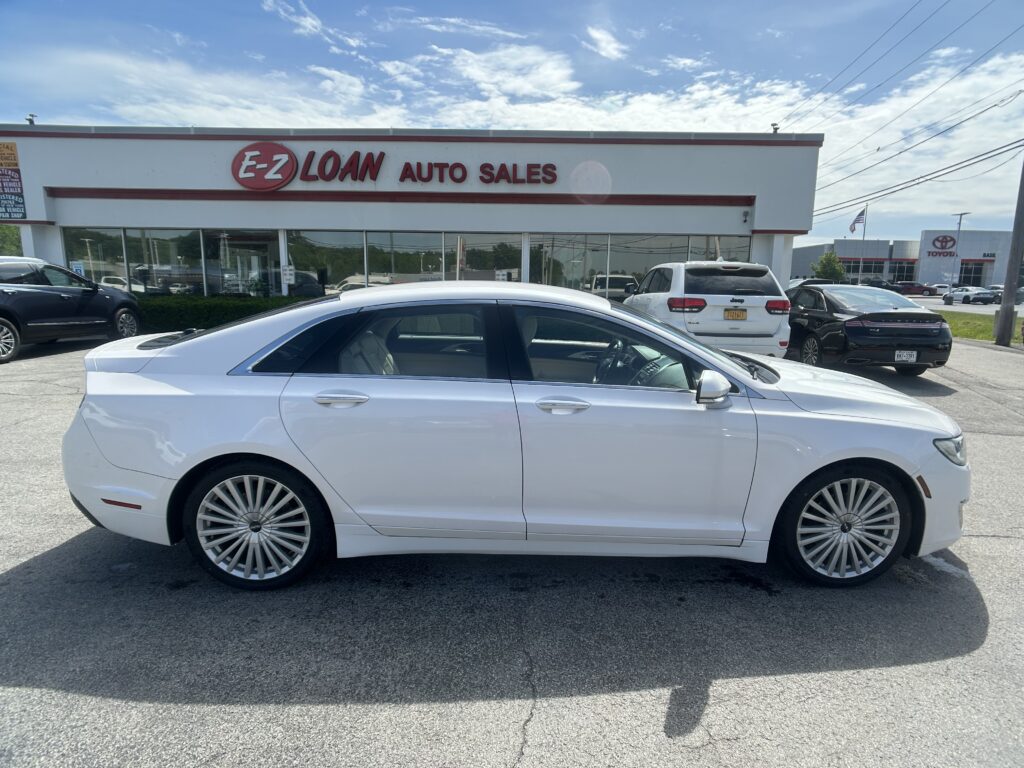 White luxury sedan parked in front of a car dealership with an E-Z LOAN Auto Sales sign and glass storefronts behind it.