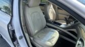 Open car door to show beige leather front seats and center console in a light-colored luxury sedan interior.