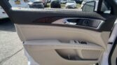 Interior of a white car door: beige leather, wood trim, chrome handle, and window control buttons; view of a busy parking lot outside with several cars.