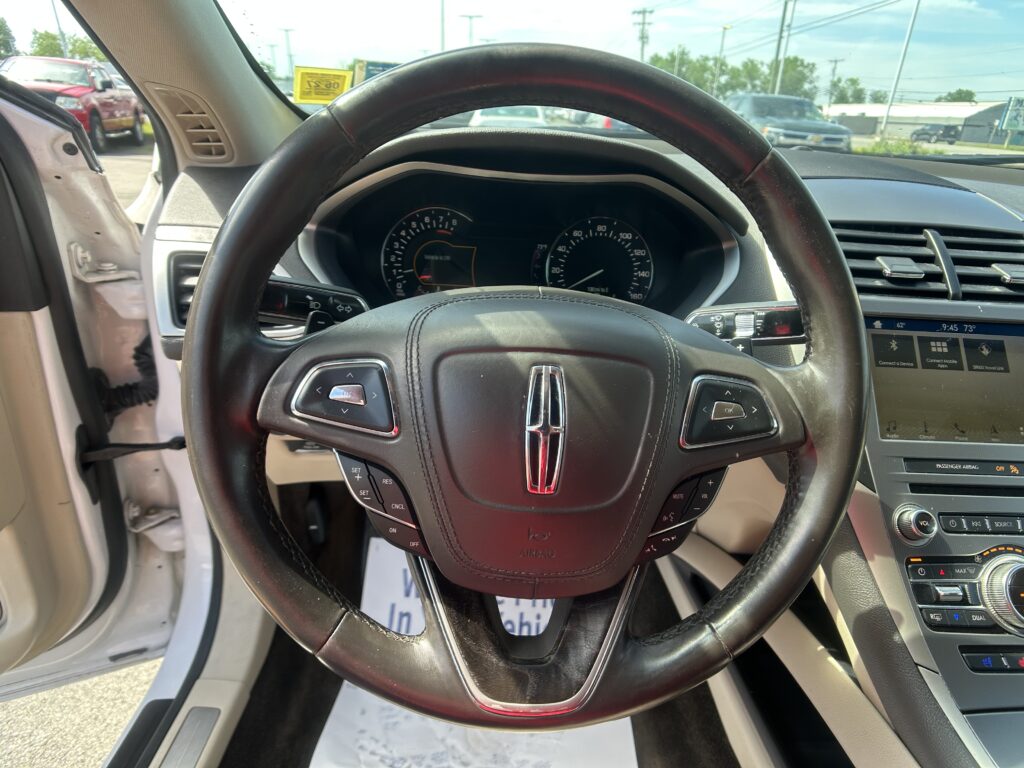Driver-view interior showing black leather steering wheel, instrument cluster, and center touchscreen on a sunny day
