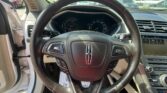 Driver-view interior showing black leather steering wheel, instrument cluster, and center touchscreen on a sunny day