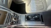 Center console controls (climate, audio) with gear selector and beige leather front seat visible in a modern car interior