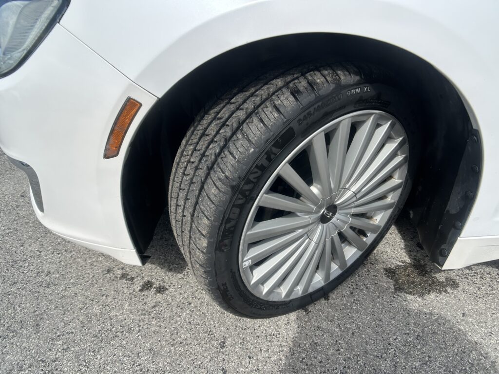 Close-up of a white car's front wheel and tire, showing a silver alloy rim and an orange side marker on the fender.