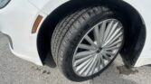 Close-up of a white car's front wheel and tire, showing a silver alloy rim and an orange side marker on the fender.